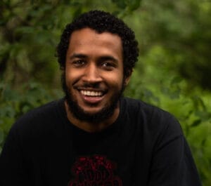 Isa sits in front of a green and heavily ferned background and is smiling