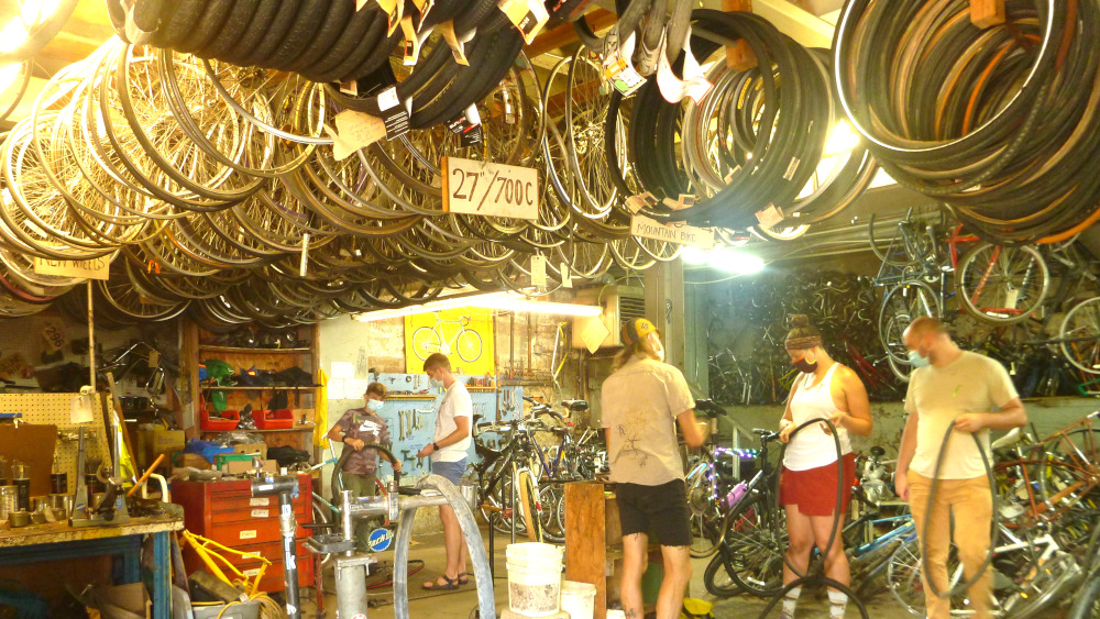 Folks working on bikes at the Asheville ReCyclery -- hundreds of bike wheels and tires hanging from the cieling throughout the space