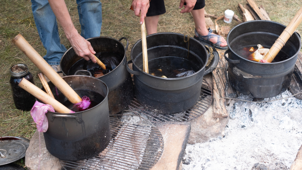 people creating natural dyes in large pots with sticks to stir