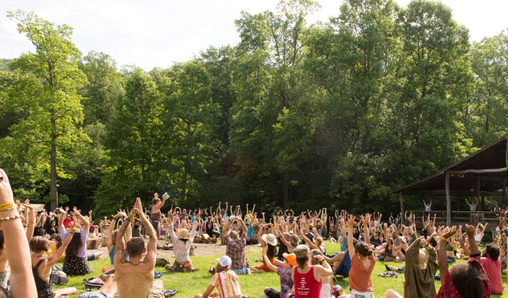 Earthskills for Everybody: Firefly Gathering's Equity Fund, Committee, and Growth 1 Gathering attendees sitting in circle while raising hands to the sky