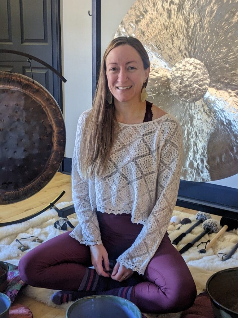 Rising Hart sits on a floor surrounded by her sound bath instruments